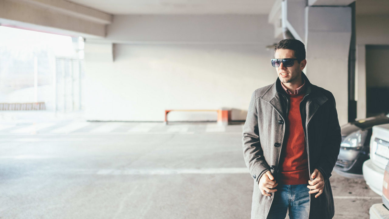 A man in a coat standing in a parking lot.