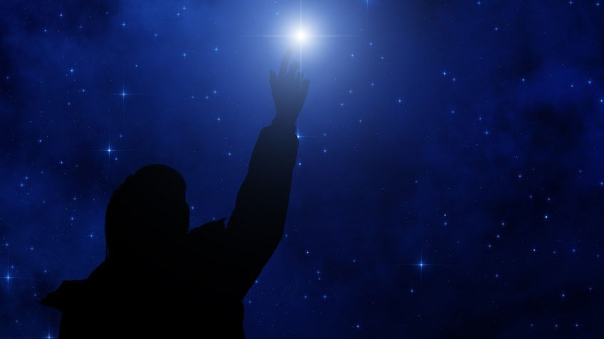 A silhouette of a person reaching for a star in the night sky.