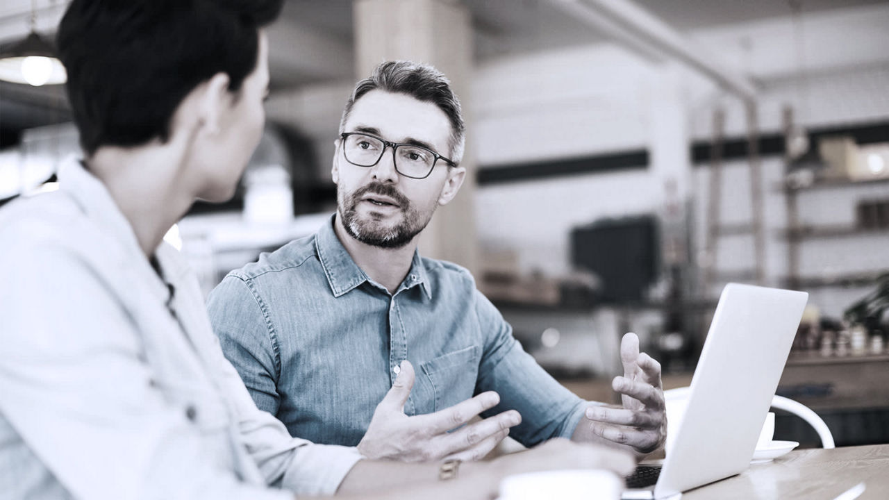 Two businessmen sitting at a table talking to each other.