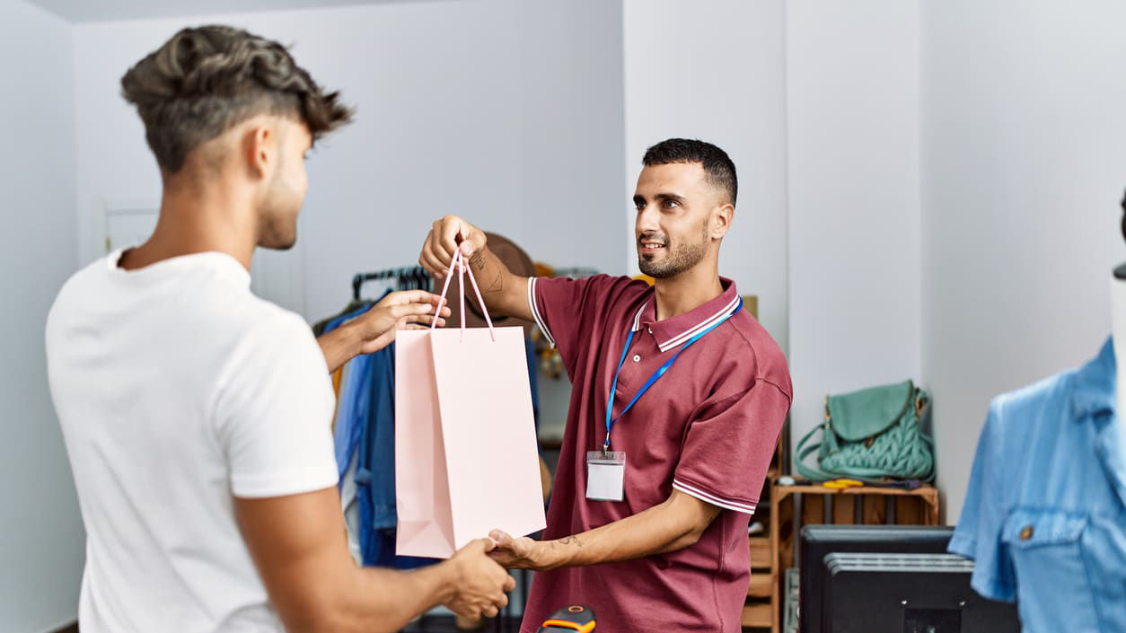 A man handing a shopping bag to another man in a store.