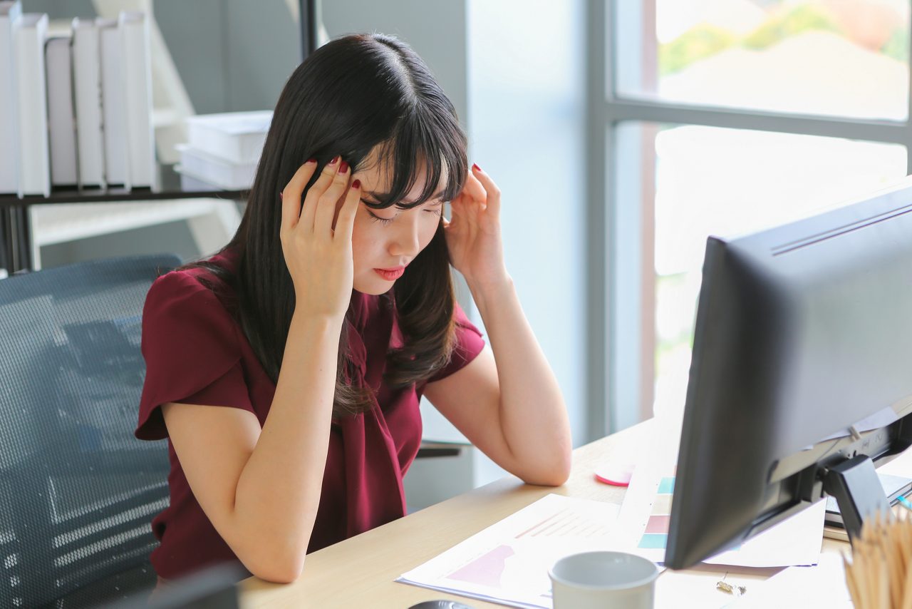 Beautiful asian woman with headache touching temples while working computer on wooden table, office syndrome and migraine image