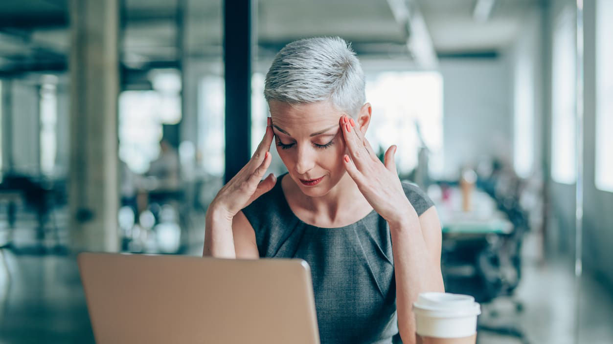A woman is sitting at a desk with a laptop and a cup of coffee.