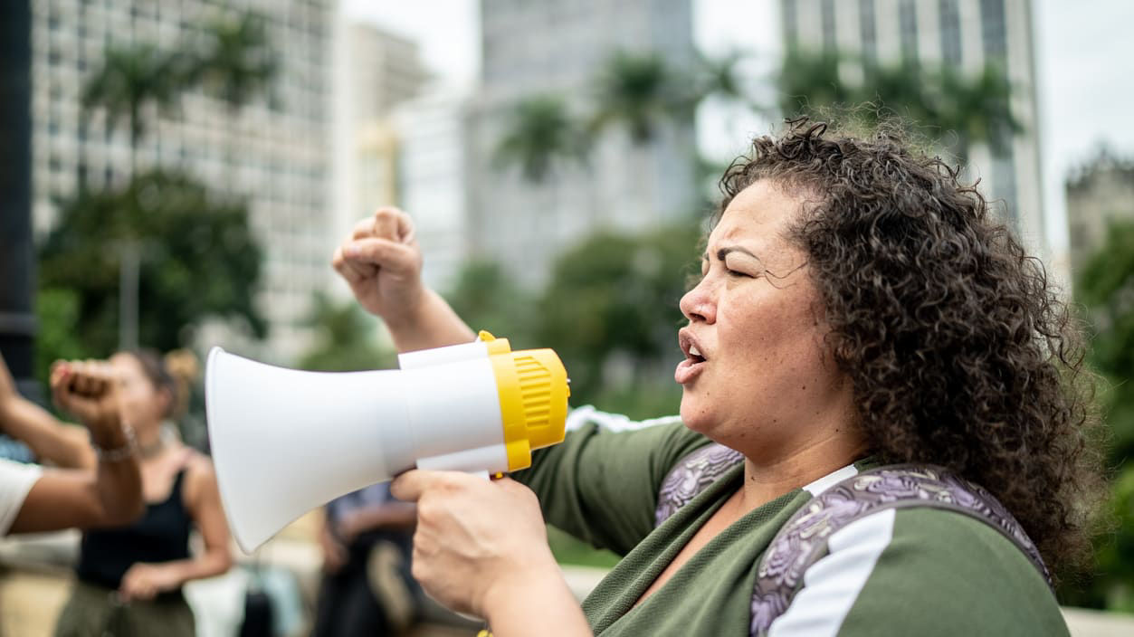 A woman shouting into a megaphone in front of a crowd of people.