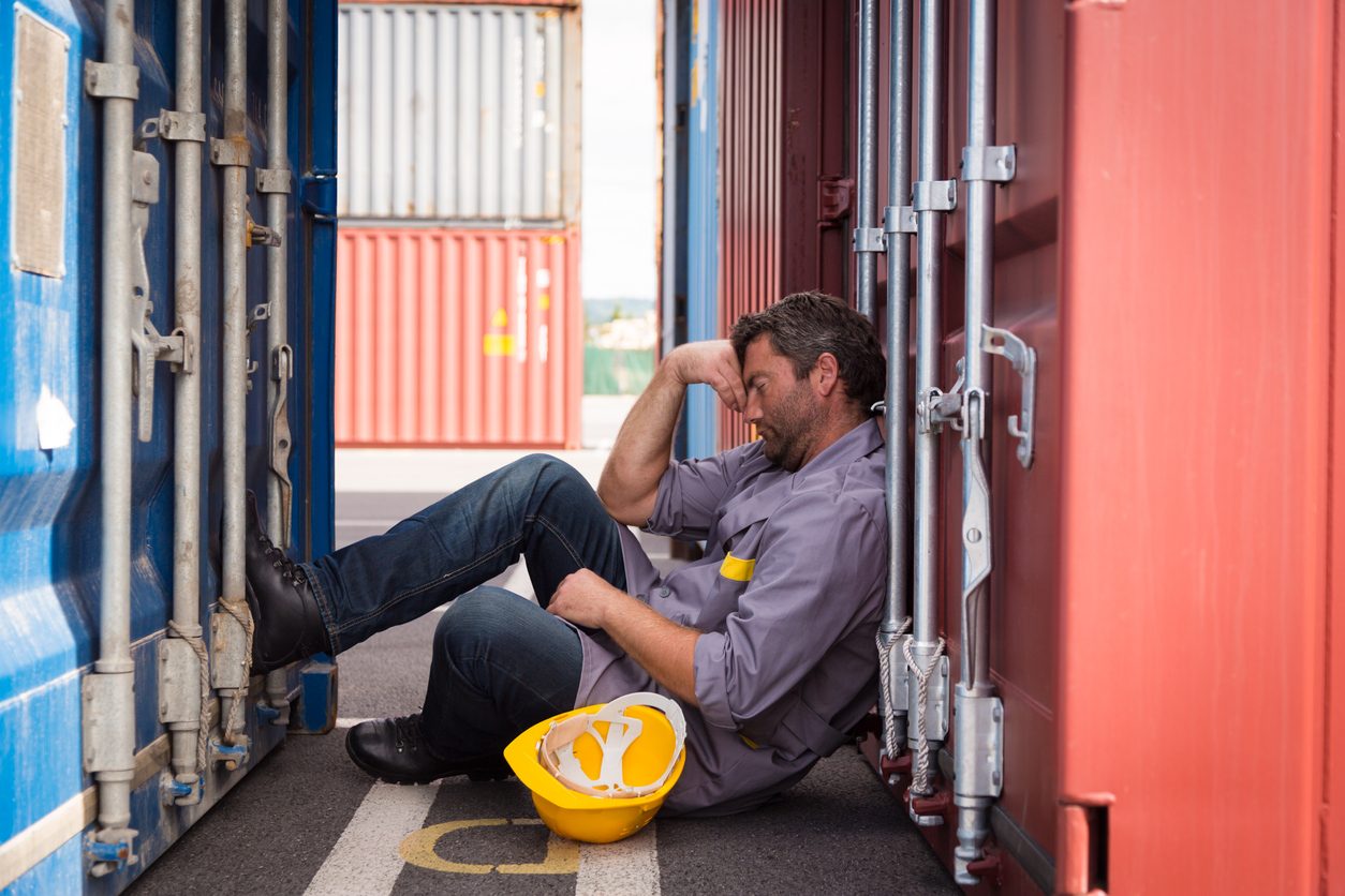 A construction worker rests with his hand on his head and his helmet off.