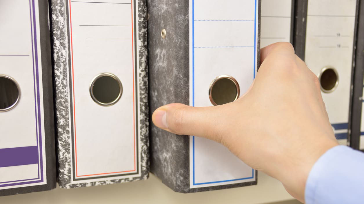 A person is holding a binder on a shelf.