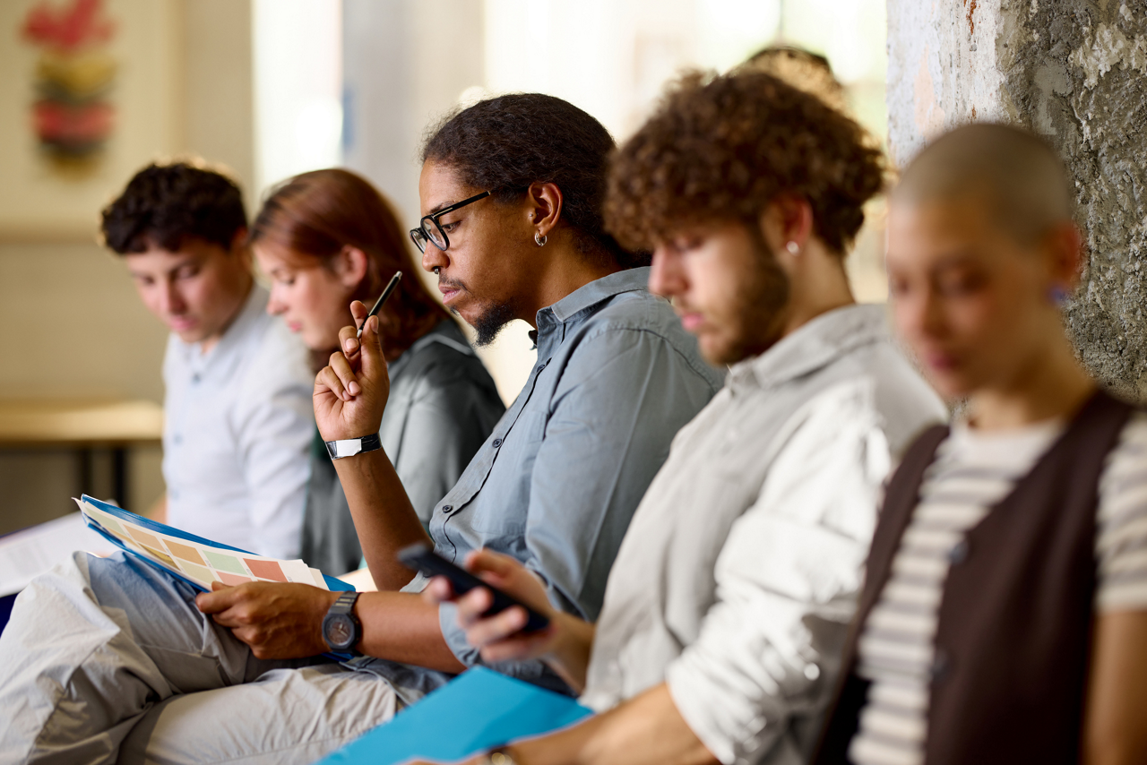 African American male entrepreneur reading reports while waiting with other candidates for a job interview in the office.