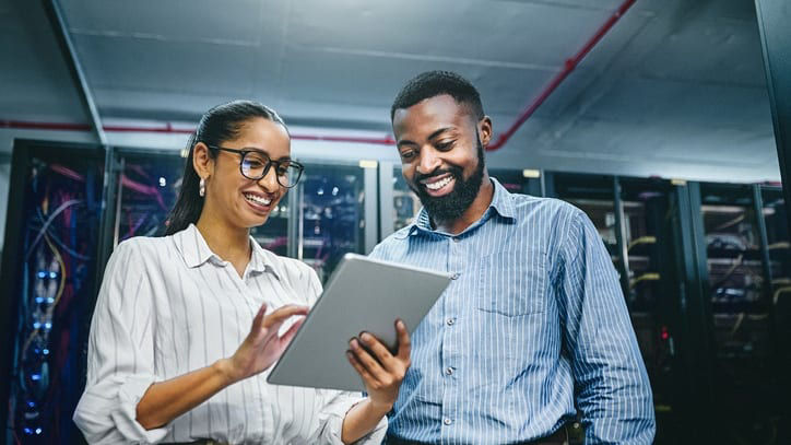 Two people in a server room looking at a tablet.