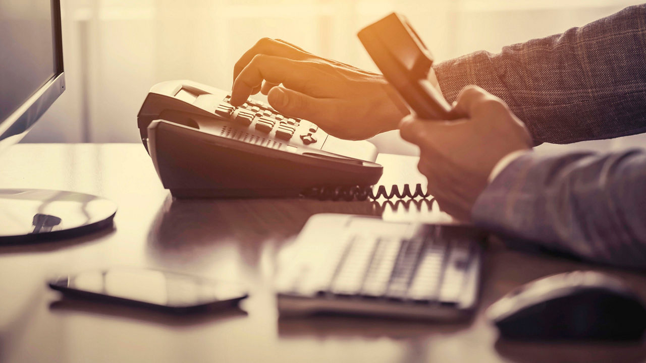 A man is using a phone while sitting at a desk.
