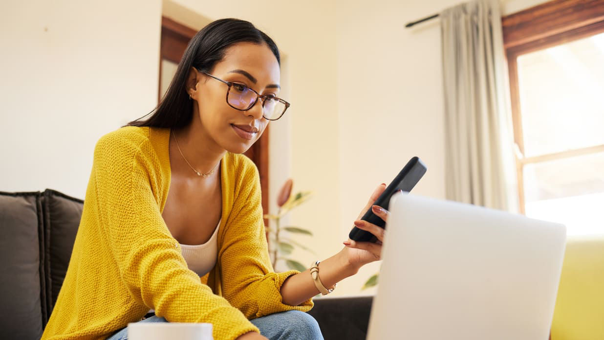 A woman sitting on a couch with a laptop and cell phone.