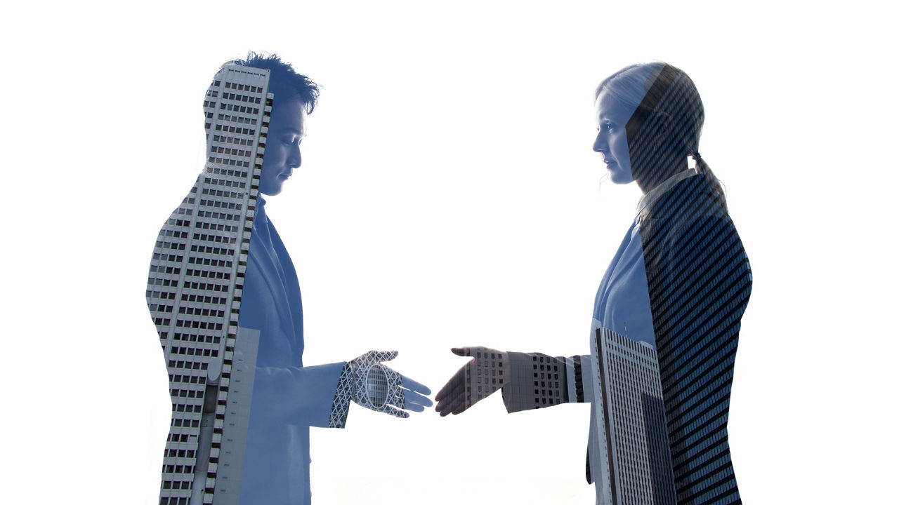 Two business people shaking hands in front of a building.