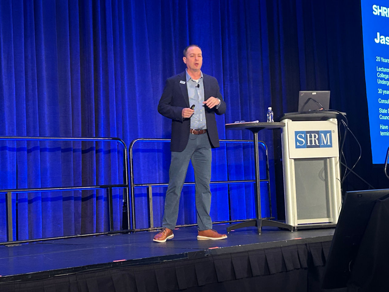 Jason Glass stands next to a podium as he presents on stage at SHRM26 in Orlando.