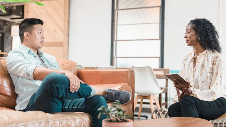 A man and woman talking on a couch in an office.