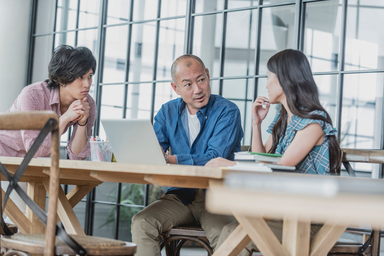 Candid portrait of there Japanese business colleagues in meeting at modern Tokyo office. Casual asian business people discussing in a creative workplace