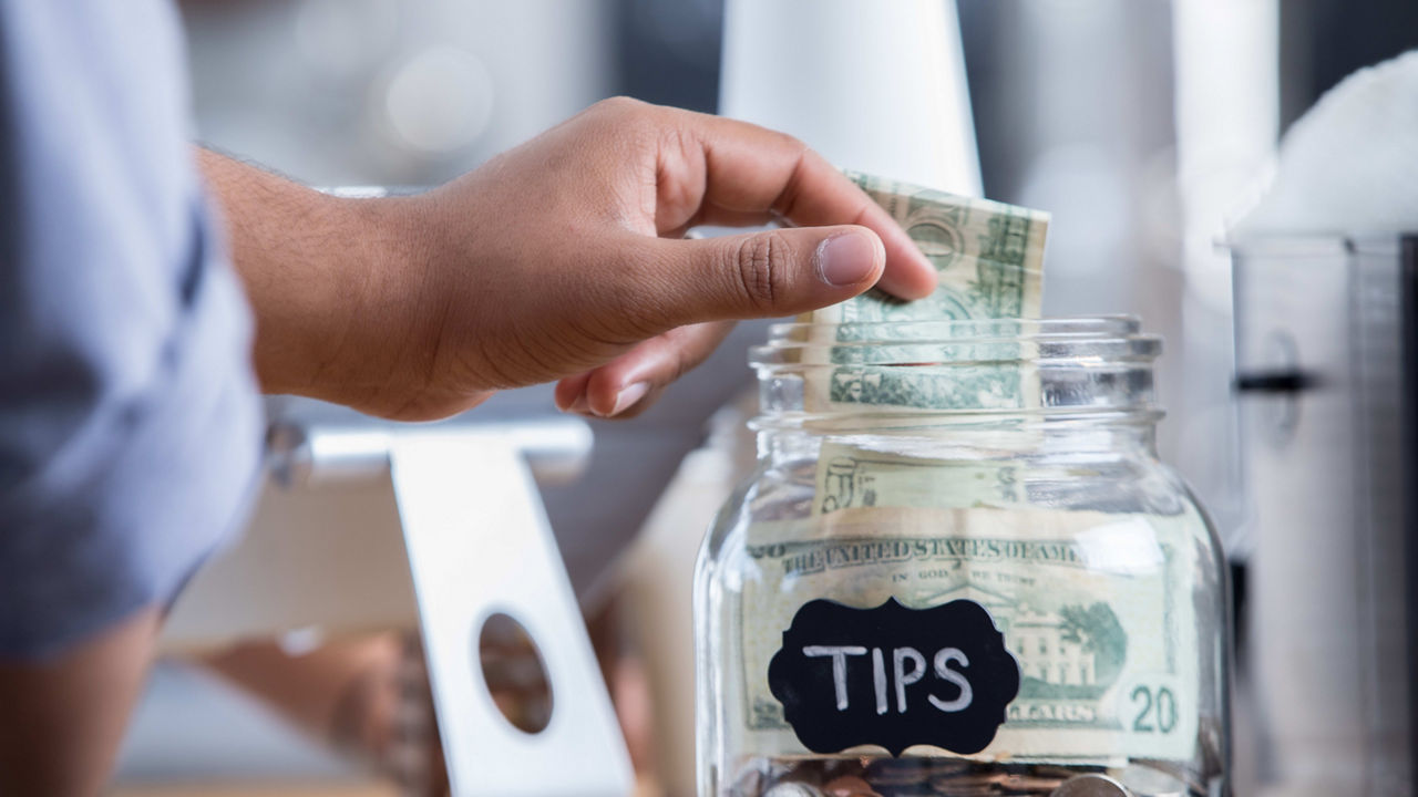 A person putting money into a glass jar.