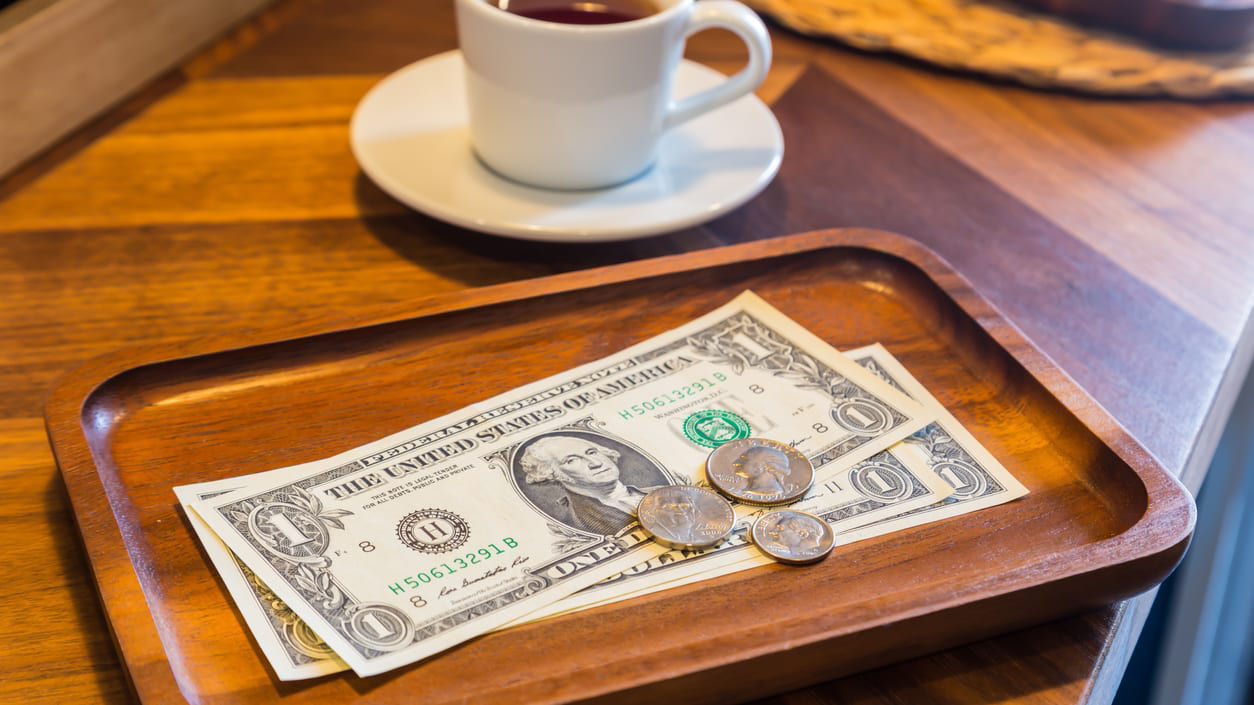 A tray with money and a cup of coffee on it.