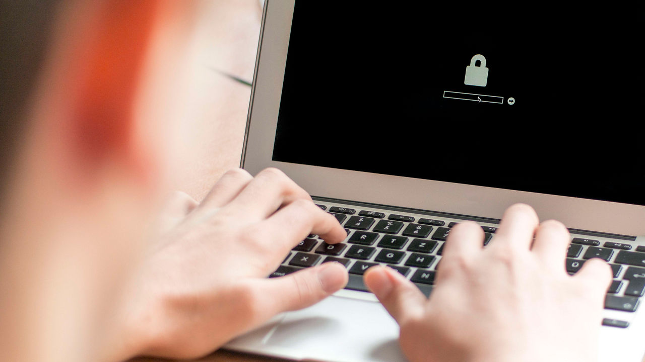 A person typing on a laptop with a padlock on it.