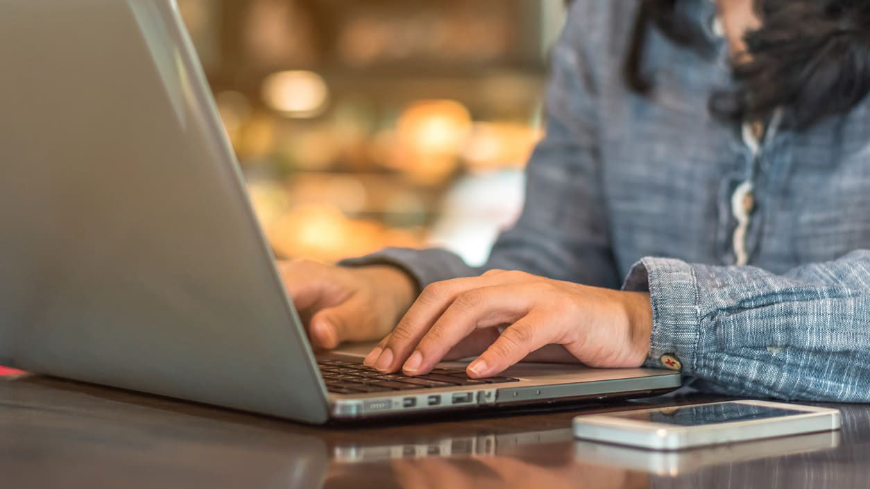 A woman is typing on a laptop at a cafe.