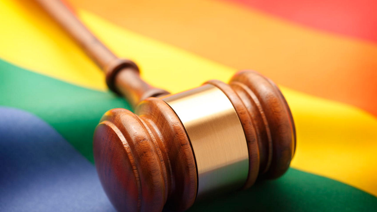 A wooden gavel on top of a rainbow flag.