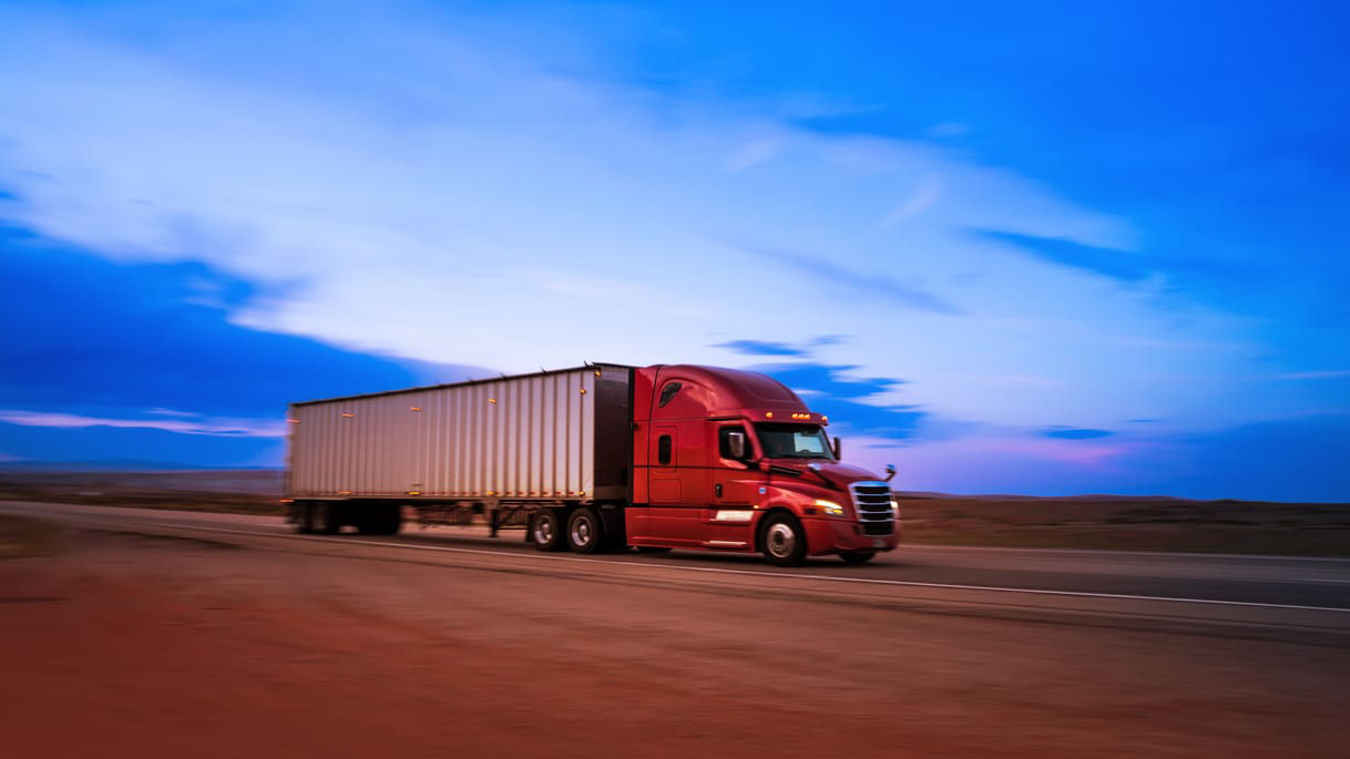 A semi truck driving down the road at dusk.
