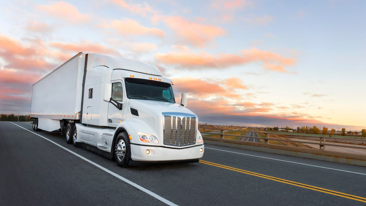 A white semi truck driving down the road at sunset.