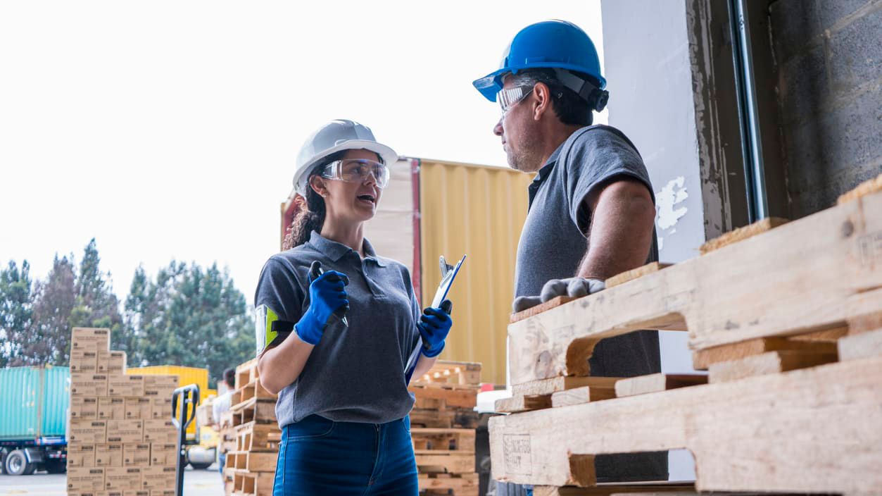 Two workers standing next to pallets in a warehouse.