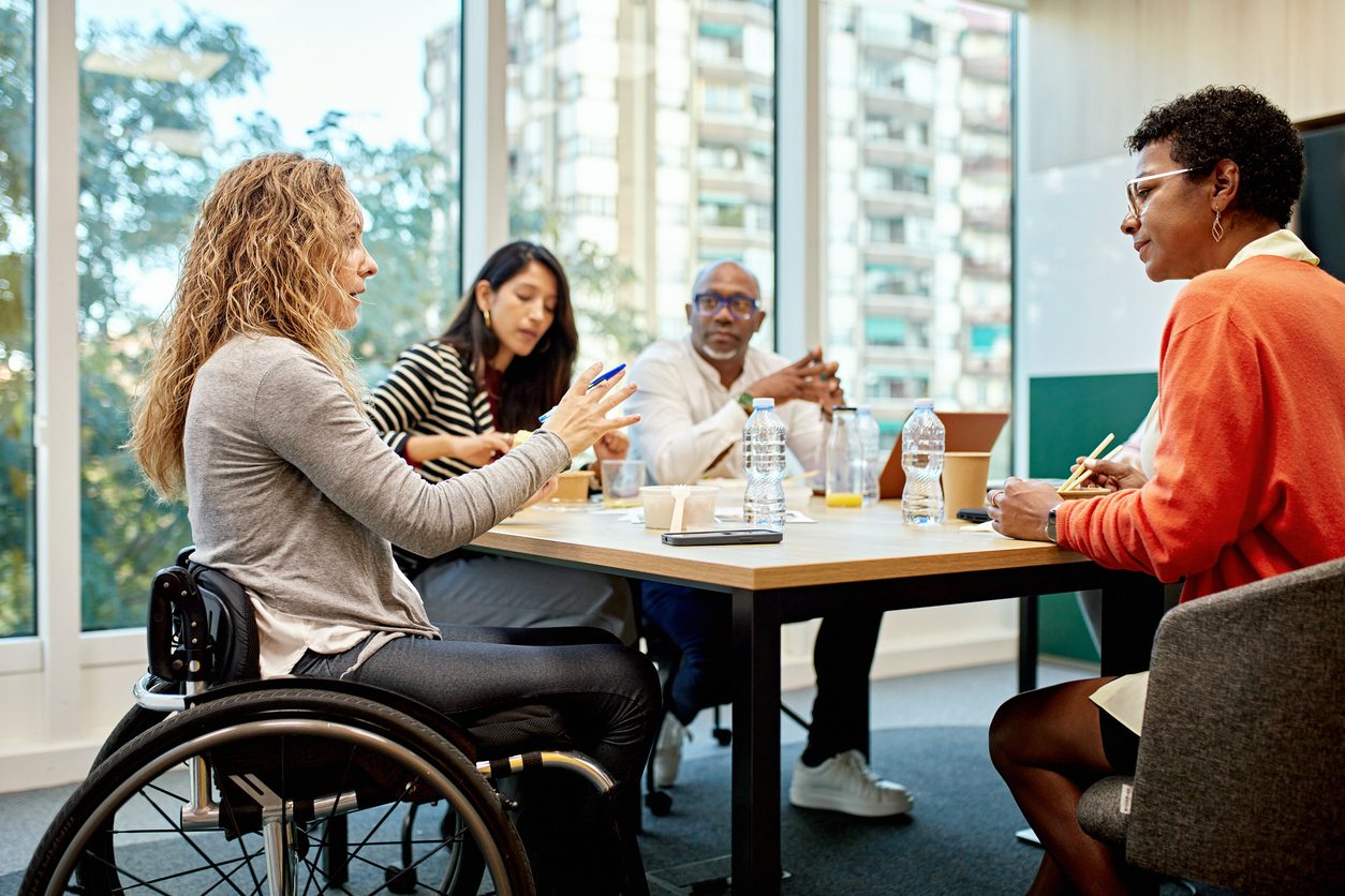 A diverse group of corporate professionals sits around a conference table and discusses ideas for project development.