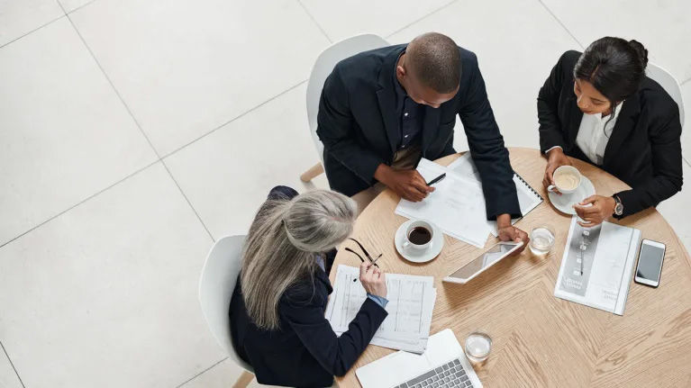 Three professionals meeting at a table over coffee.