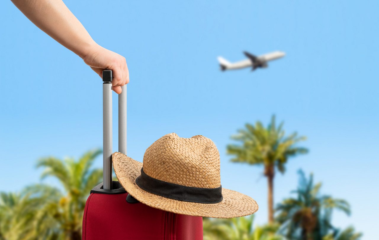 closeup of a suitcase and a sun hat with an airplane in the background