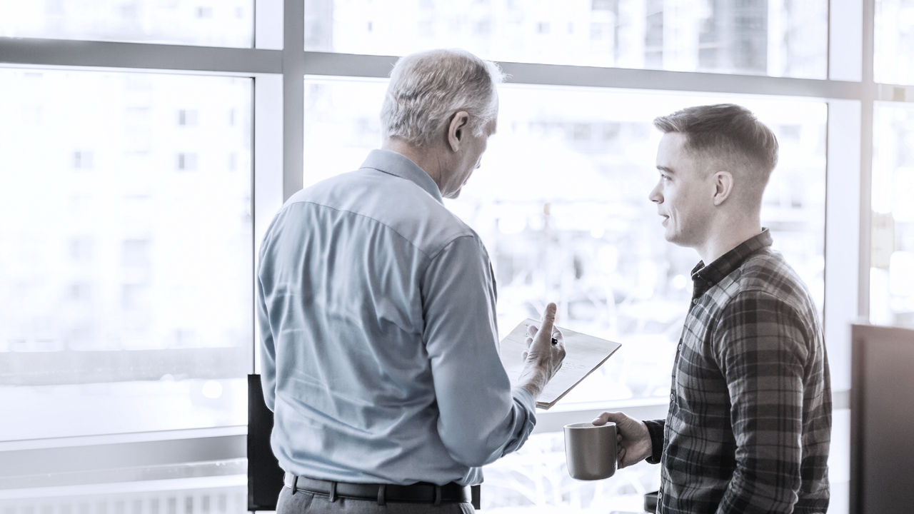 Two employees standing next to each other, one holding mug, the other looking at document