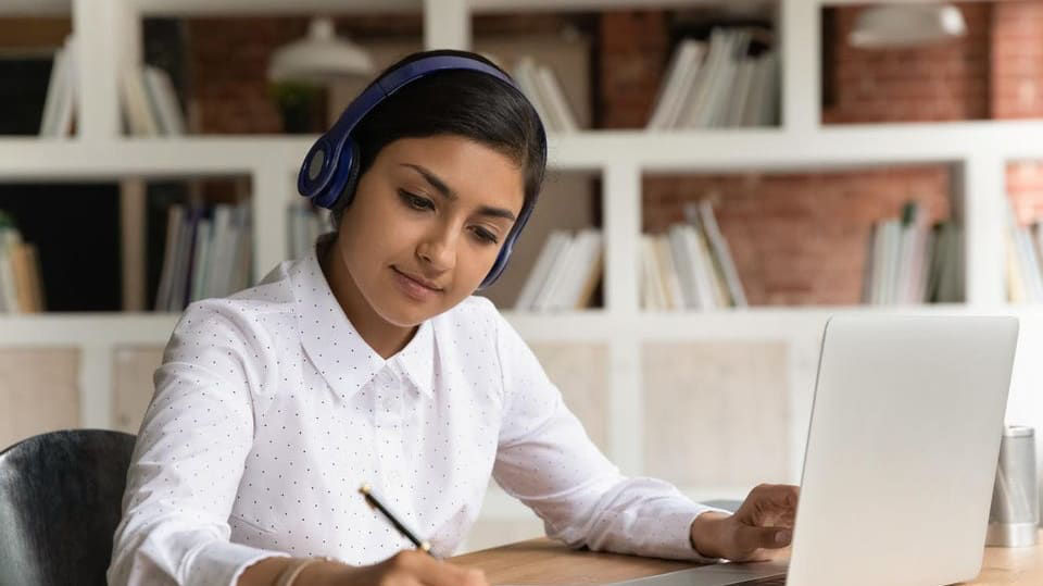 A woman wearing headphones is sitting at a desk with a laptop.