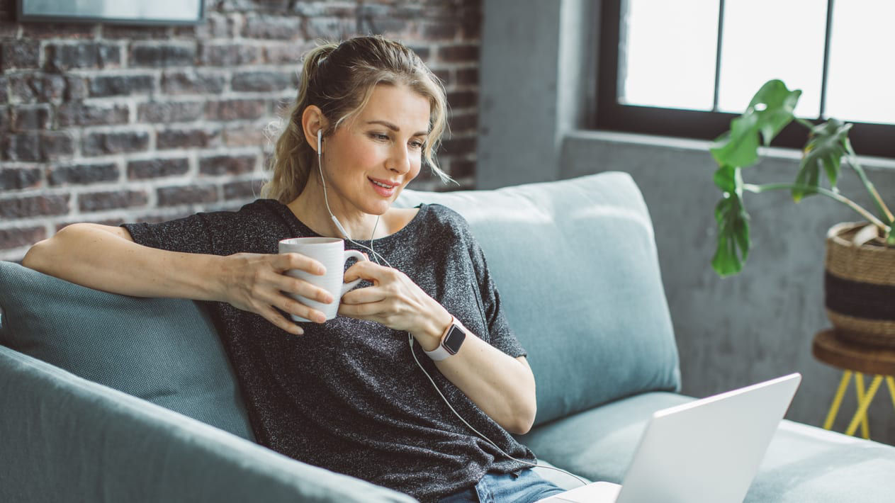 A woman sitting on a couch with a laptop and a cup of coffee.