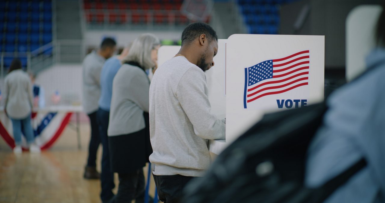 People standing at voting booths with dividers on election day.