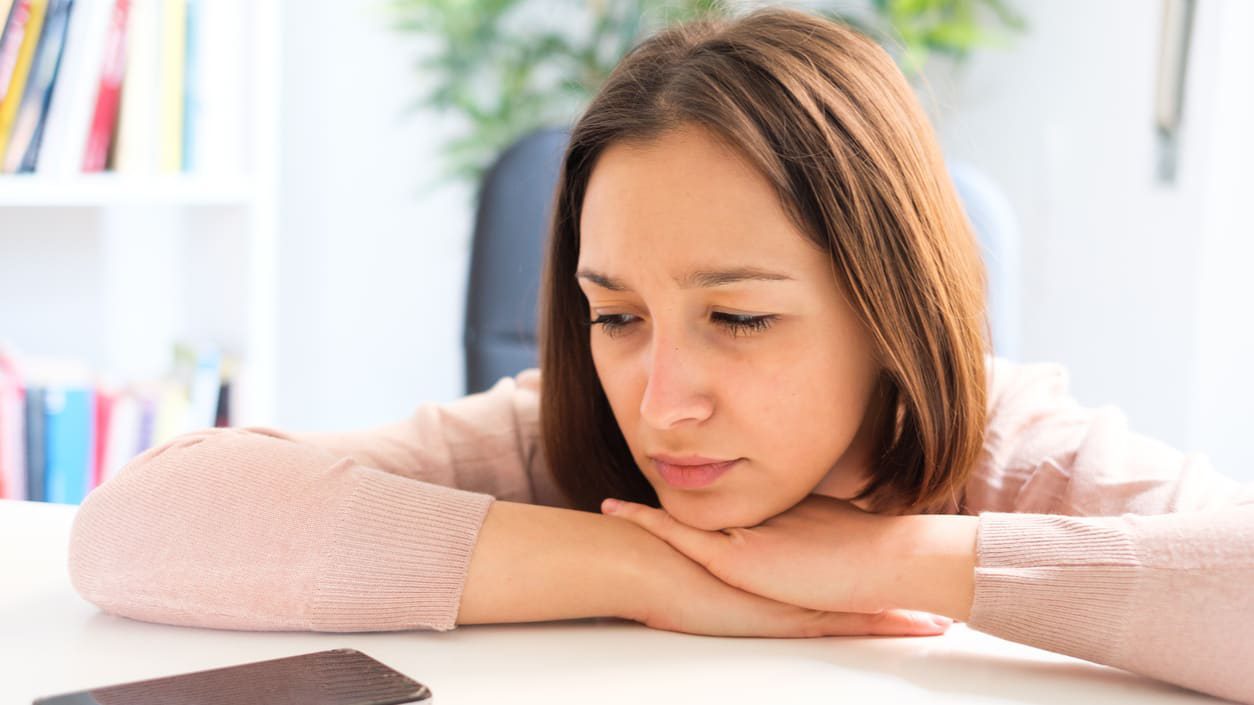 A woman is sitting at a desk looking at her phone.