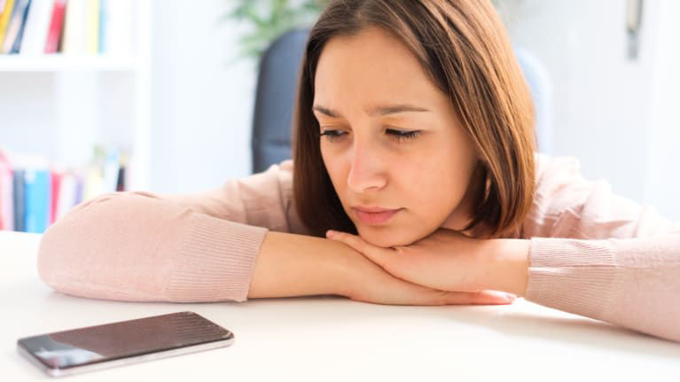 A woman is sitting at a desk looking at her phone.