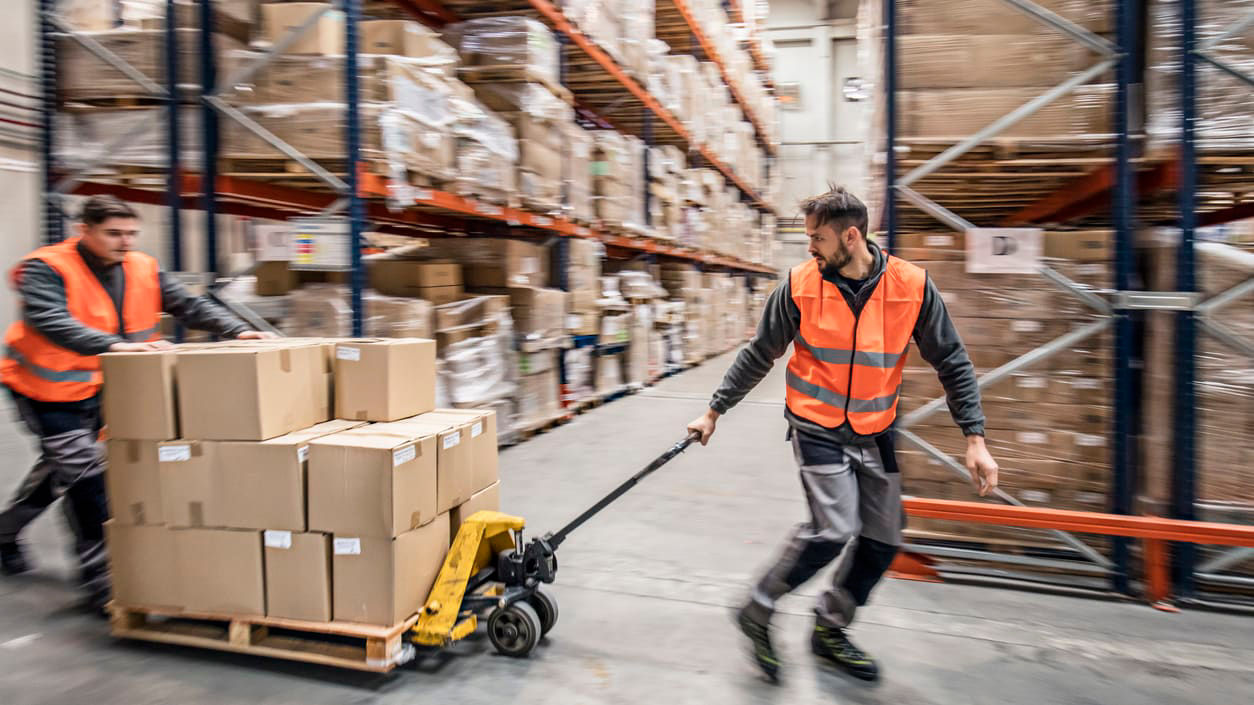 Two warehouse workers pushing boxes in a warehouse.
