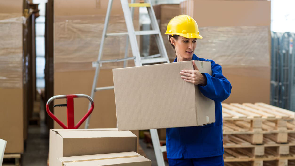 A man in a hard hat holding a box in a warehouse.