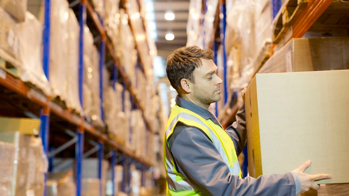A warehouse worker picking up a box in a warehouse.