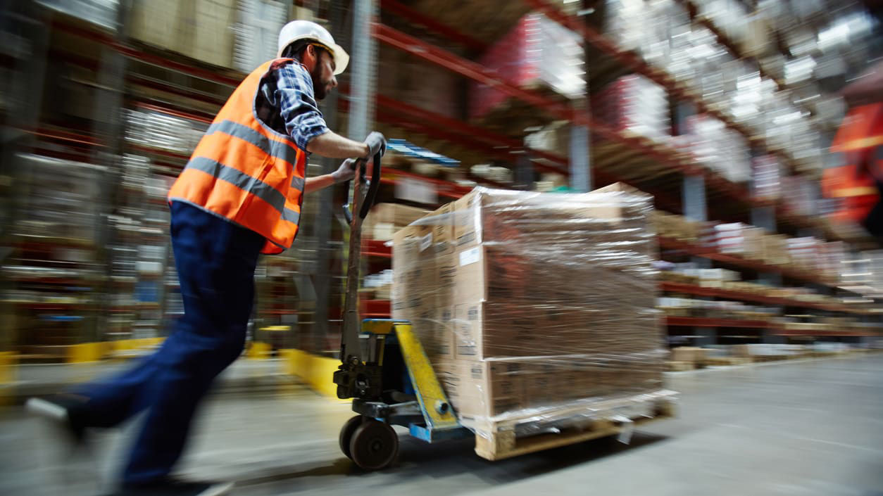 A worker is pushing a pallet in a warehouse.