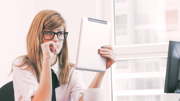 A woman in glasses sitting at a desk with a tablet.