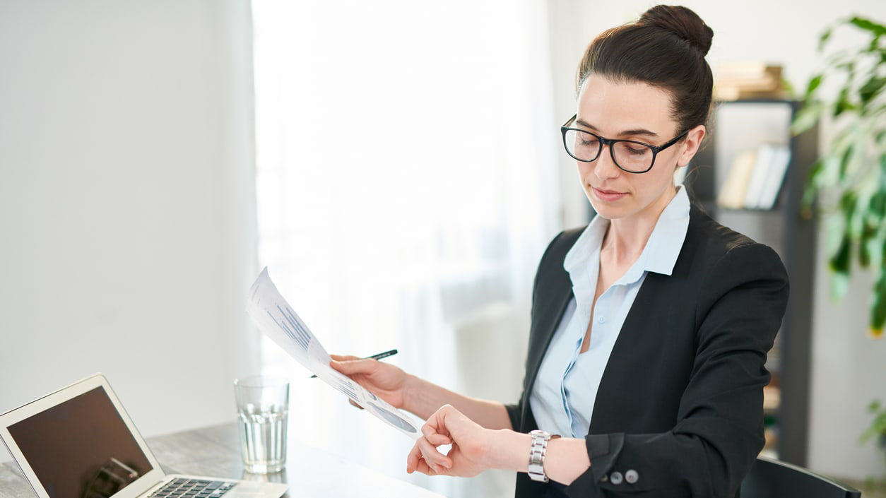 A business woman is sitting at a desk with papers and a laptop.