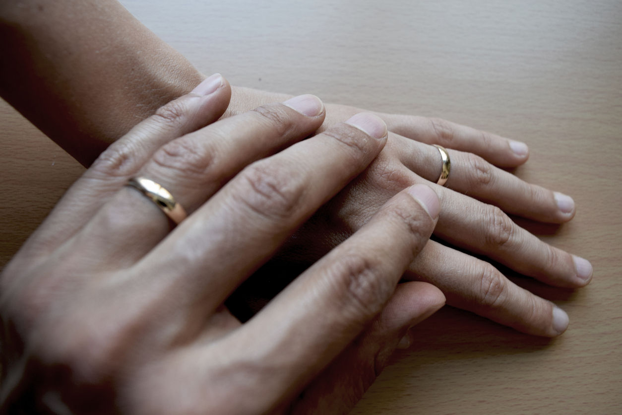 Two people holding hands wearing wedding rings.