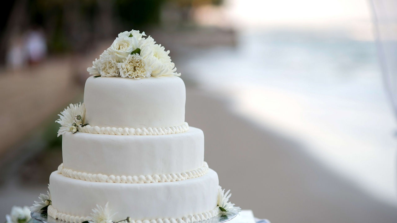 A white wedding cake sits on a table near the beach.