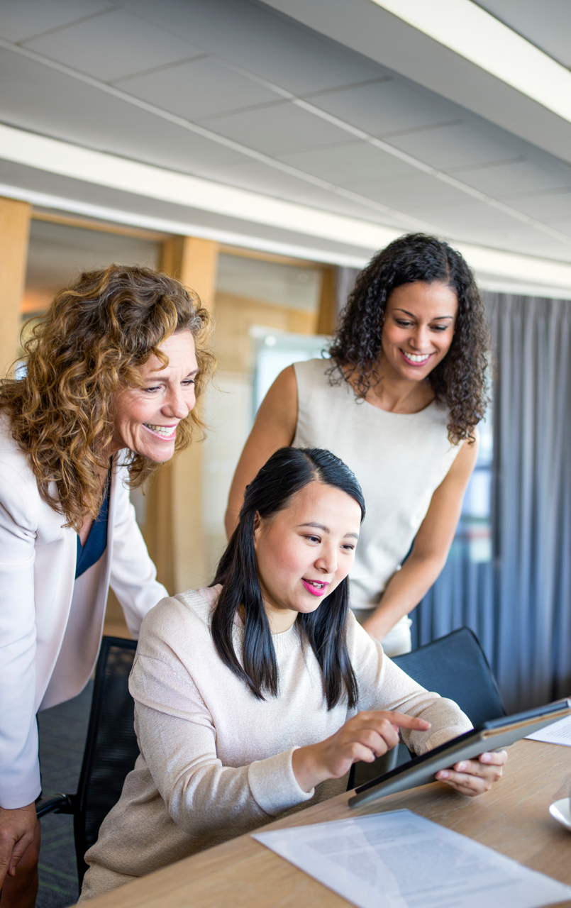 Smiling colleagues looking while businesswoman using digital tablet in board room. Female professionals are discussing in meeting at workplace. They are working at corporate office.