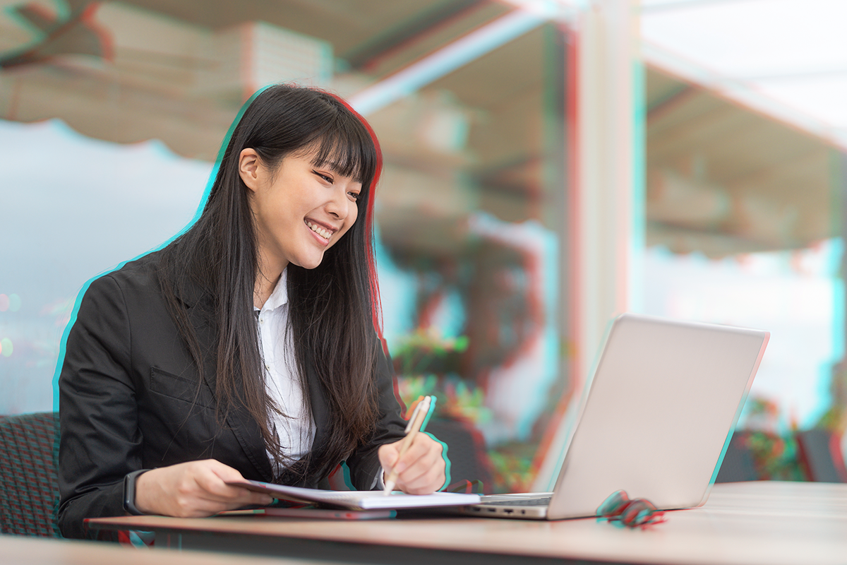 woman writing on notepad on top of laptop