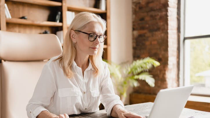 A woman in glasses is using a laptop in her office.