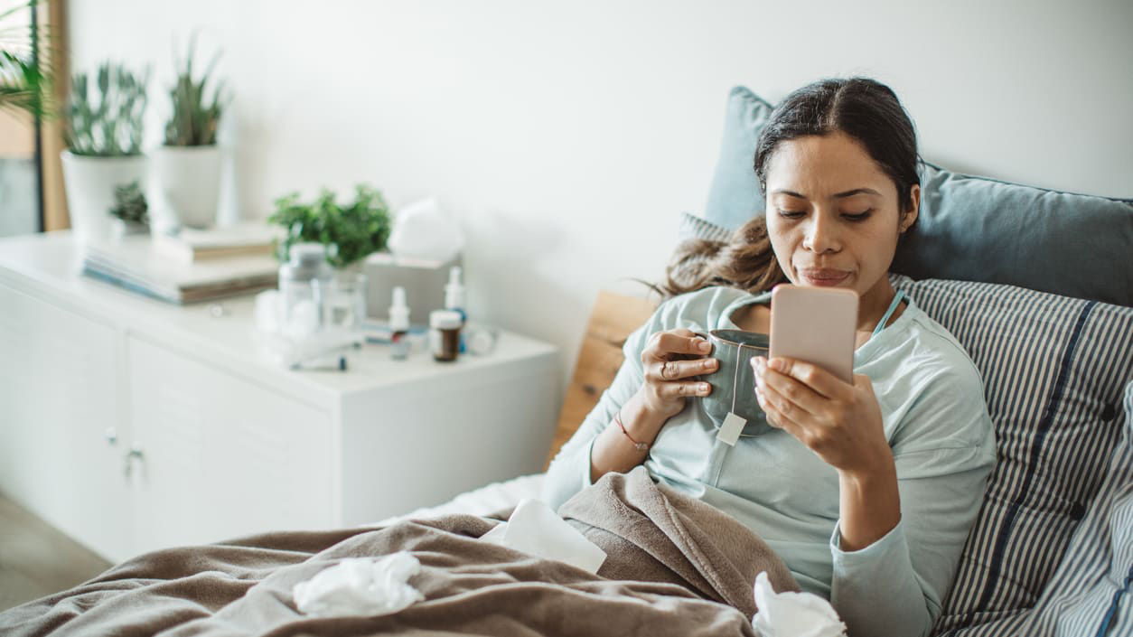 A woman is sitting in bed with a cup of coffee and a tissue.