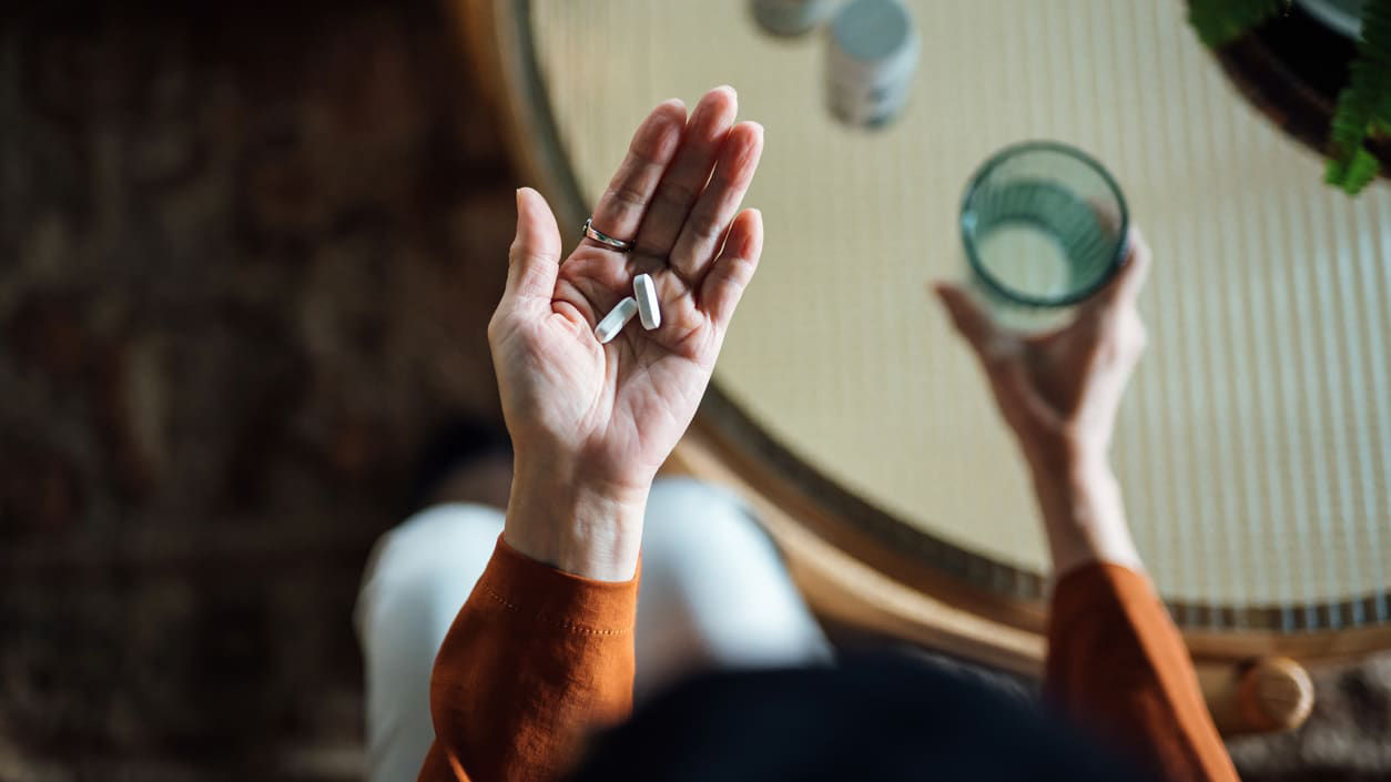 A woman holding a pill while sitting at a table.