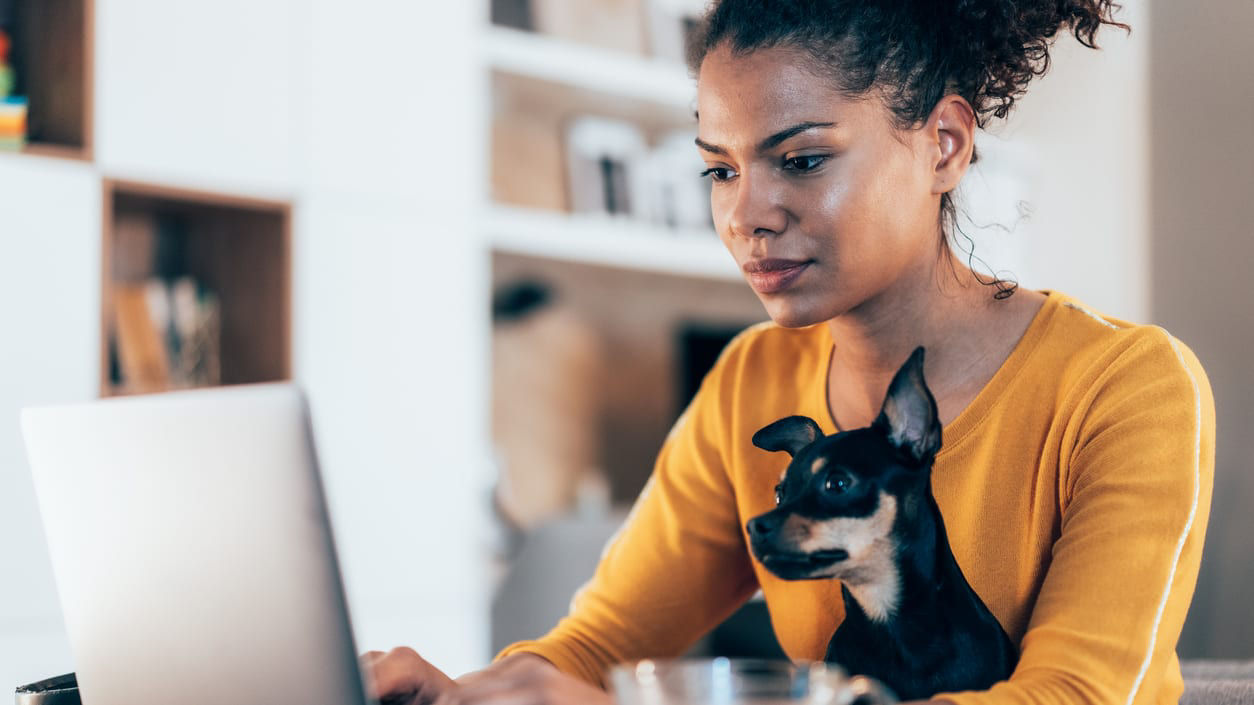 A woman using a laptop with a dog on her lap.