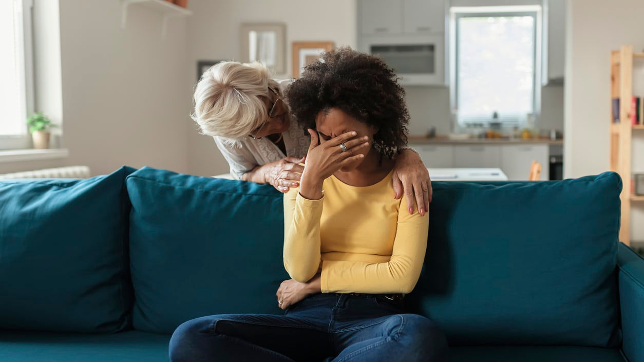 A woman is sitting on a couch with her hands on her face.