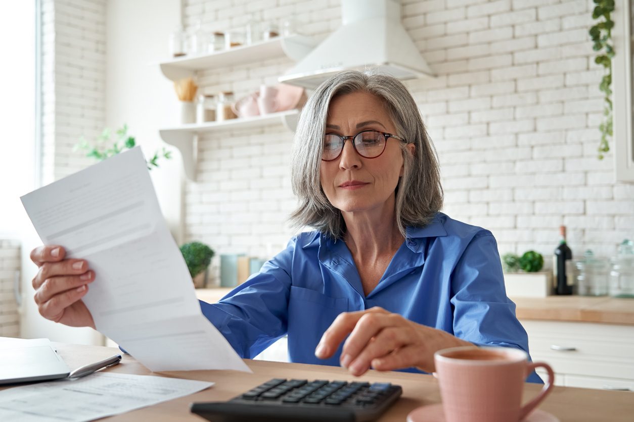 Woman at a table looking at a bill or financial document and by a calculator